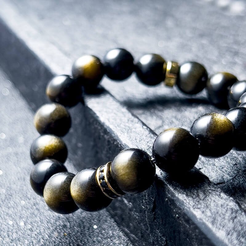 Man in gothic attire wearing Gold Sheen Obsidian bracelet for Root Chakra protection and dark luxury style