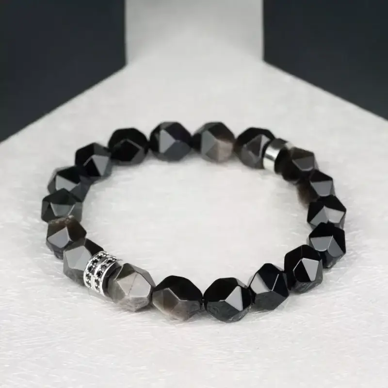 Close-up of hand wearing Natural Obsidian & Silver Sheen Bracelet against a rocky landscape – symbolizes earth’s enduring protection and inner security, offering calm resilience through life’s challenges.